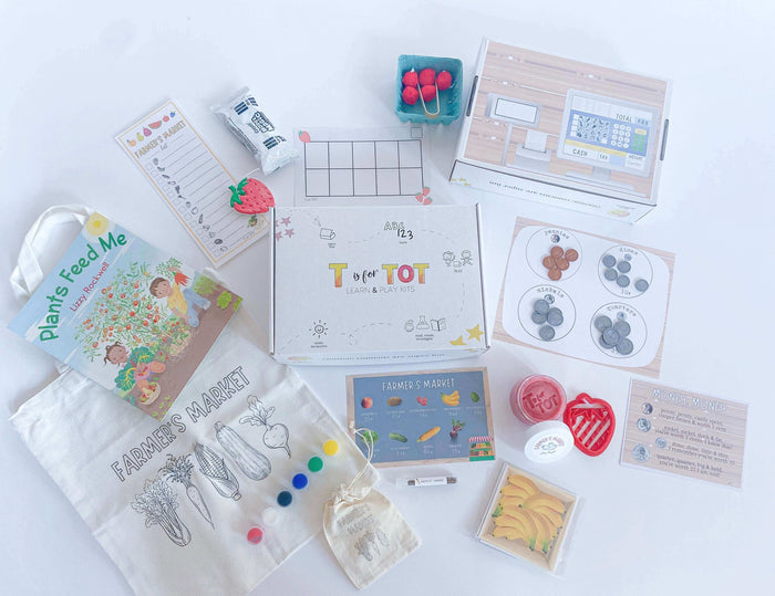 Interactive Farmer's Market play kit for kids with strawberry-scented playdough, custom strawberry cutter, pretend cash register, play money, and a canvas tote bag for painting. Includes 'Plants Feed Me' book and a tens frame math game.