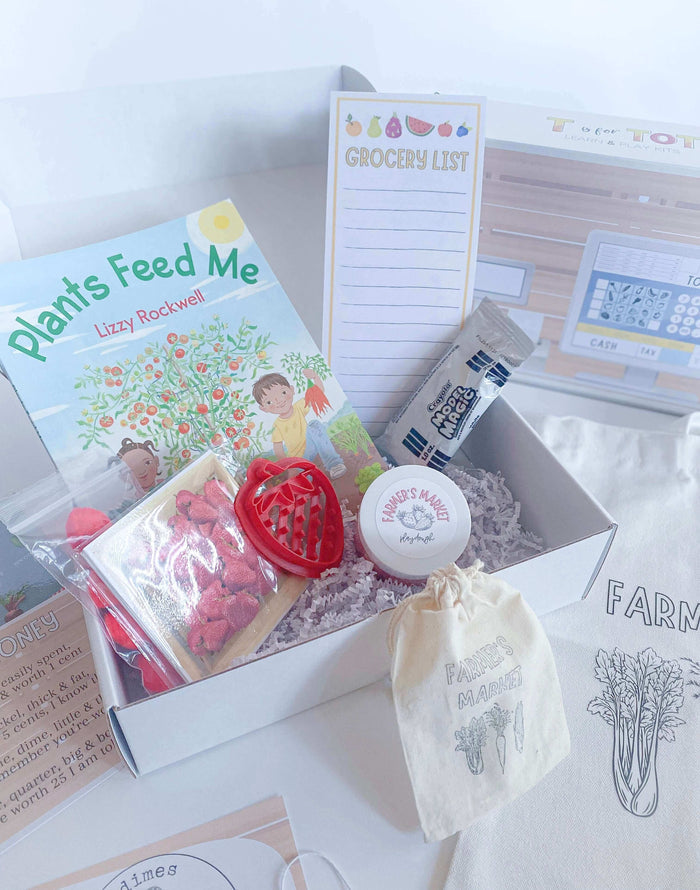Play and learn Farmer's Market kit featuring strawberry-scented playdough, custom cutter, canvas tote bag with paint, play money, and a pretend cash register. Includes 'Plants Feed Me' book, tens frame math game, and steam & recipe cards.