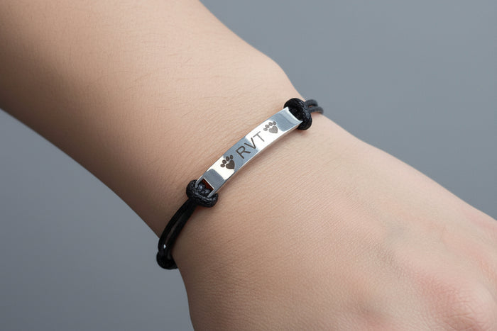 Black cord bracelet with a metal tag on that says RVT with paw prints