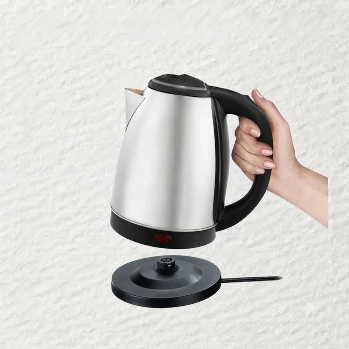A hand holding a stainless steel electric kettle with a black handle and base, shown above its matching black power base on a light textured background.